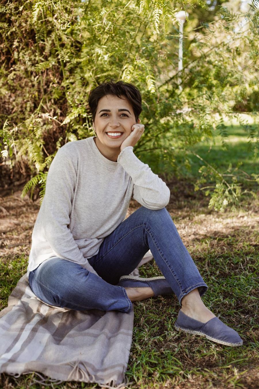 Grazielle sentada sobre uma manta na grama, sorrindo